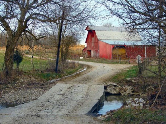 image of a red barn, gravel road, and two trees